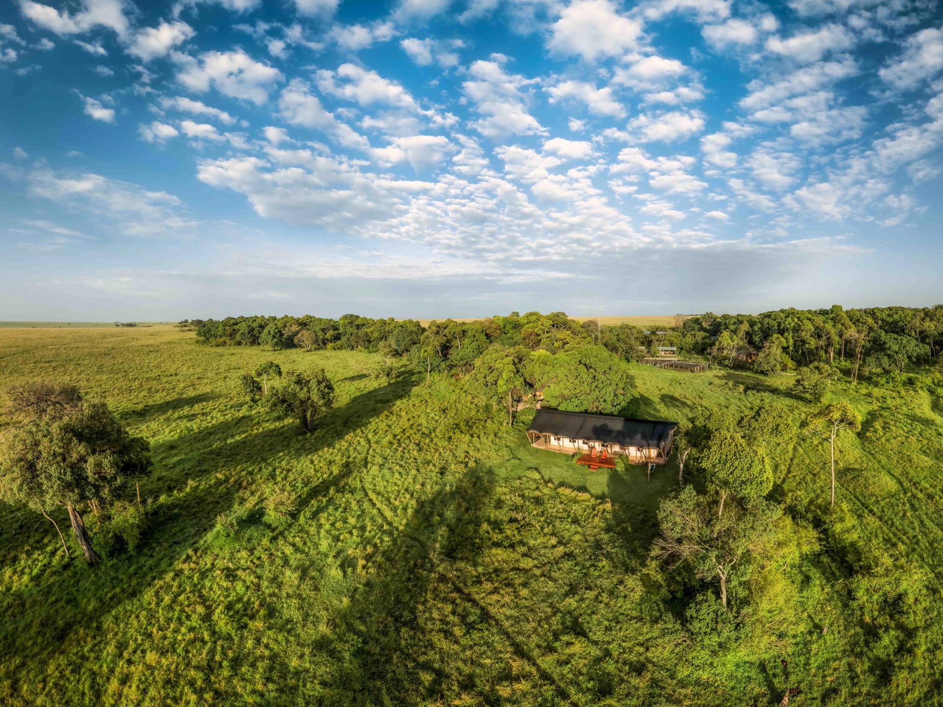 An aerial view of a camp set in green bush with open country beyond
